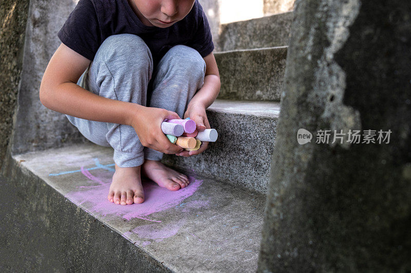 小男孩用紫色粉笔在外面的水泥地板上画画