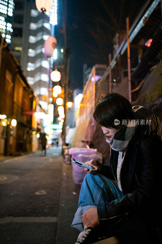 坐在漆黑的居酒屋街上的年轻女子