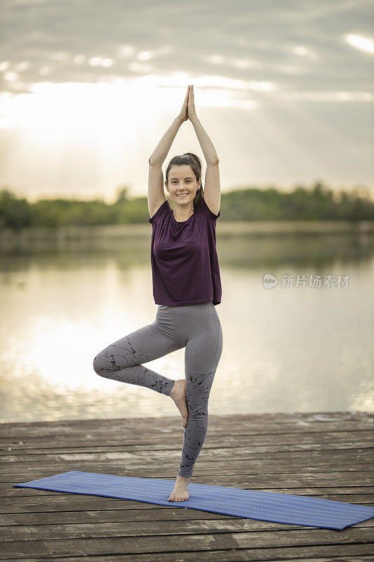 年轻的运动有吸引力的女人练习瑜伽，在湖码头做Vrksasana锻炼