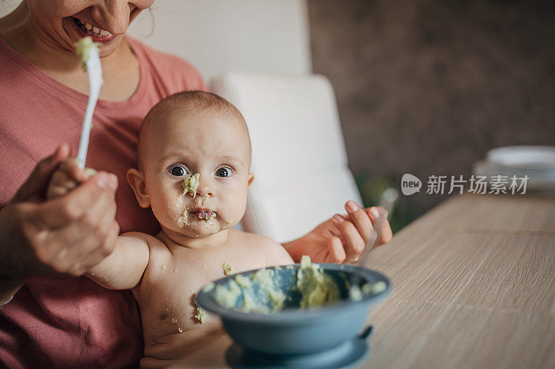 年轻的母亲试图用勺子喂养婴儿的儿子