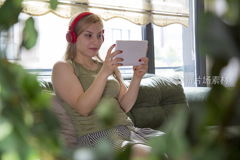女人戴着耳机在起居室里使用平板电脑