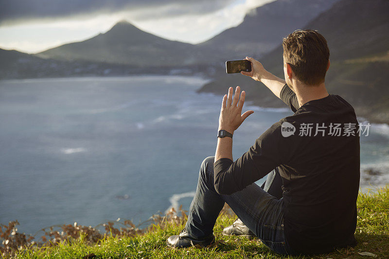 坐在悬崖边用智能手机的男人。