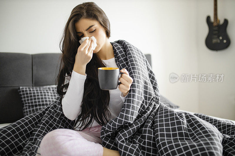 睡着的生病的小女孩躺在床上，感冒和高烧，喝着茶