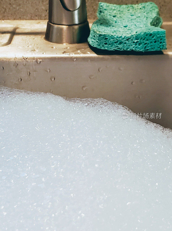 厨房水槽里的肥皂用用过的绿色海绵产生泡沫