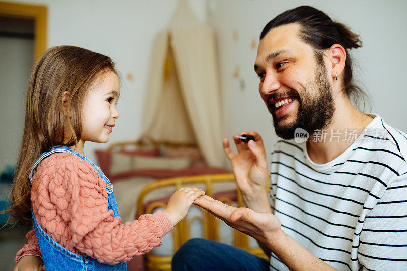 年轻的父亲在家给小女儿涂指甲