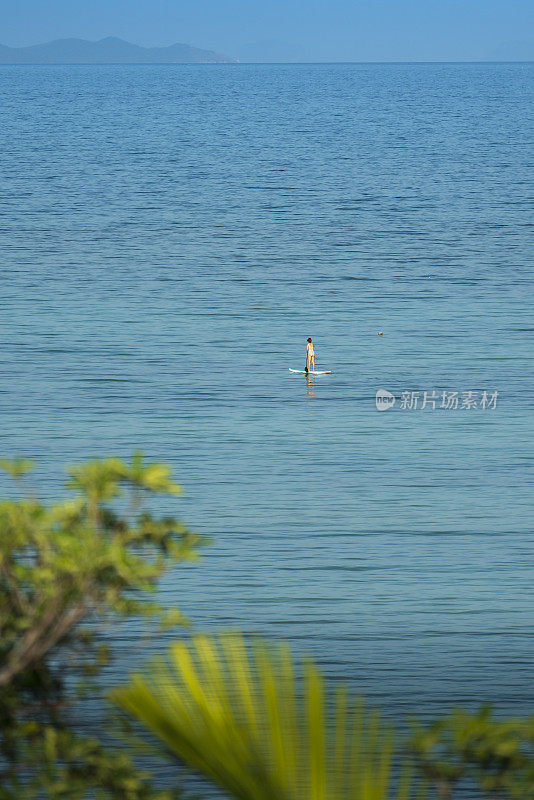 在泰国普吉岛的潘瓦海滩上，一名女子站起来，用桨冲浪过海