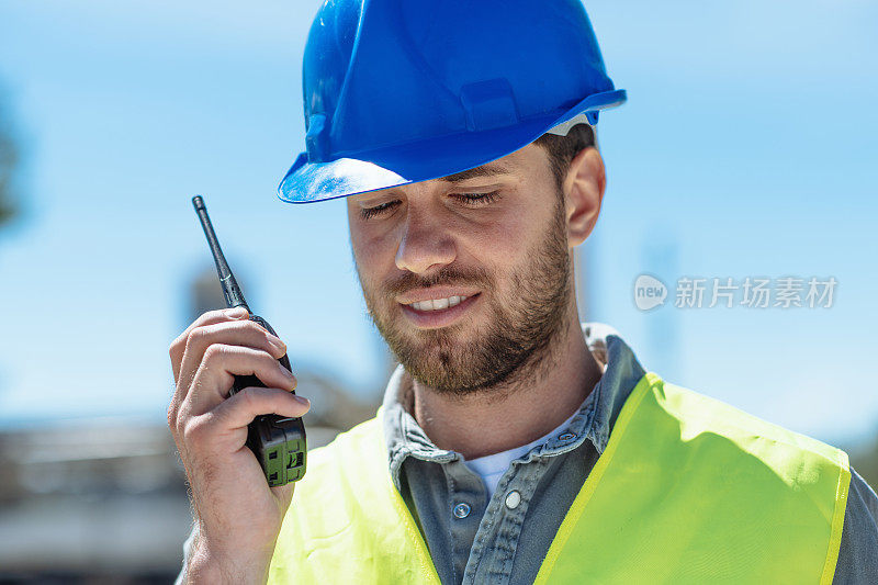 带安全帽的工程师在建筑工地-用对讲机的人的特写