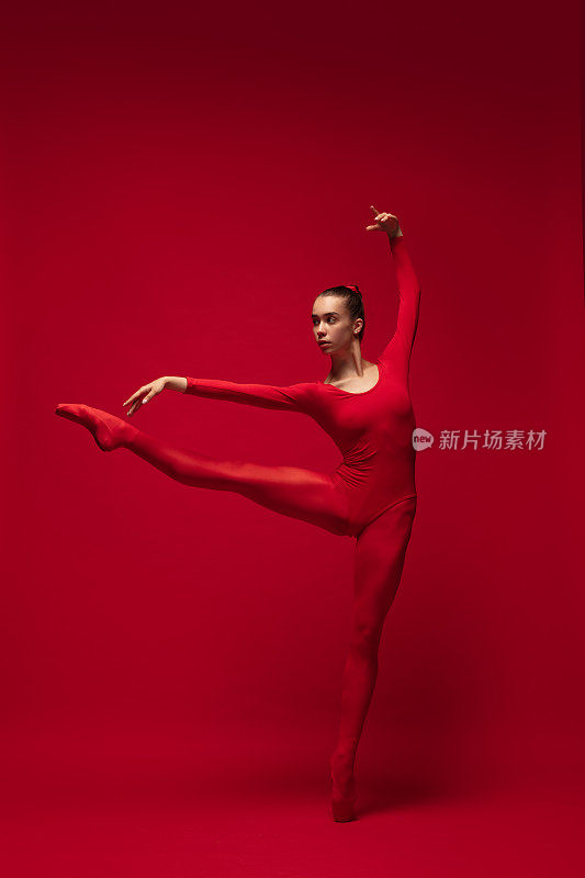 优雅的年轻美丽的女孩，女芭蕾舞者摆出孤立的红色背景。