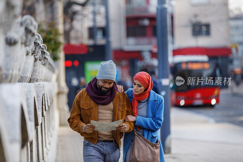 年轻的非洲男子和他的穆斯林妻子带着旅游地图在市区散步。