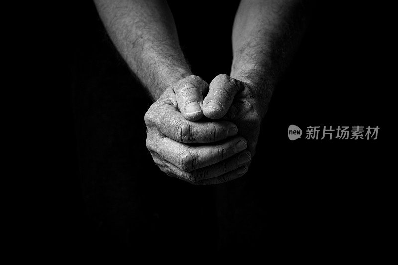 男性伸出双手，紧握在一起沉思或祈祷。