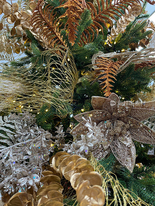 人工特写图像，金色的桉树树叶，银色的树叶，挂在人造圣诞树树枝上的金色花头饰品，云杉针，模糊的白色神仙灯背景