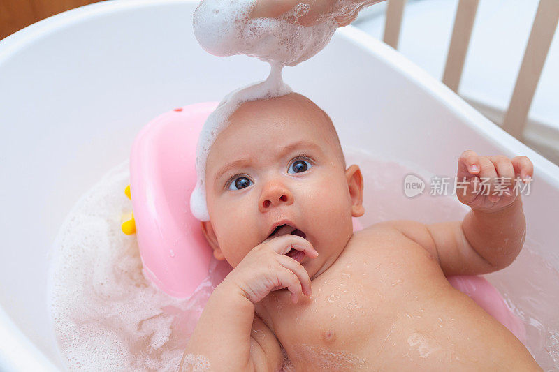 婴儿在浴缸里洗澡，泡沫在他的头上