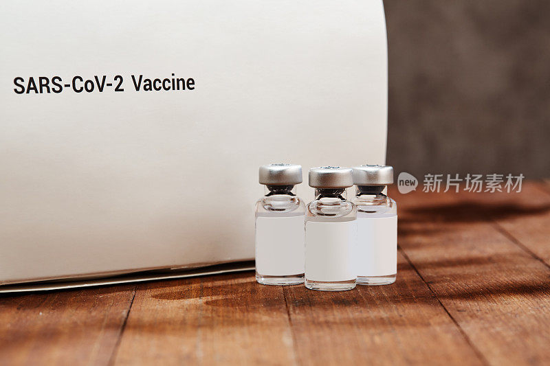 木桌上放着几瓶SARS-CoV-2疫苗，阳光下有阴影
