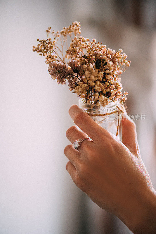 女人们手上戴着钻石戒指，手里拿着玻璃罐里的干花