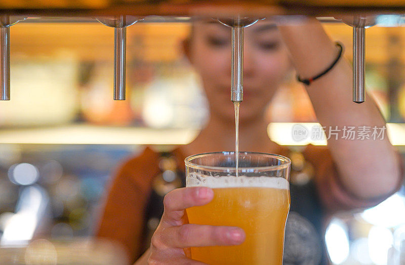 酒吧女酒保手握啤酒龙头，将生啤酒倒入玻璃杯中