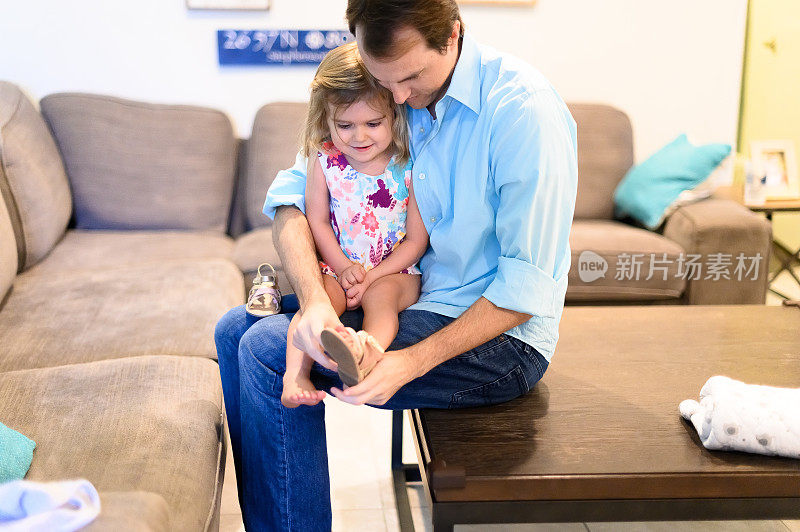 父亲在客厅为蹒跚学步的女儿穿上鞋子