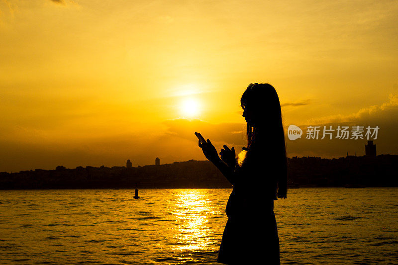 日落时使用手机的美丽女孩的剪影