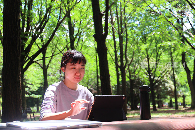 一个年轻女子坐在公园的户外，手里拿着一台笔记本电脑