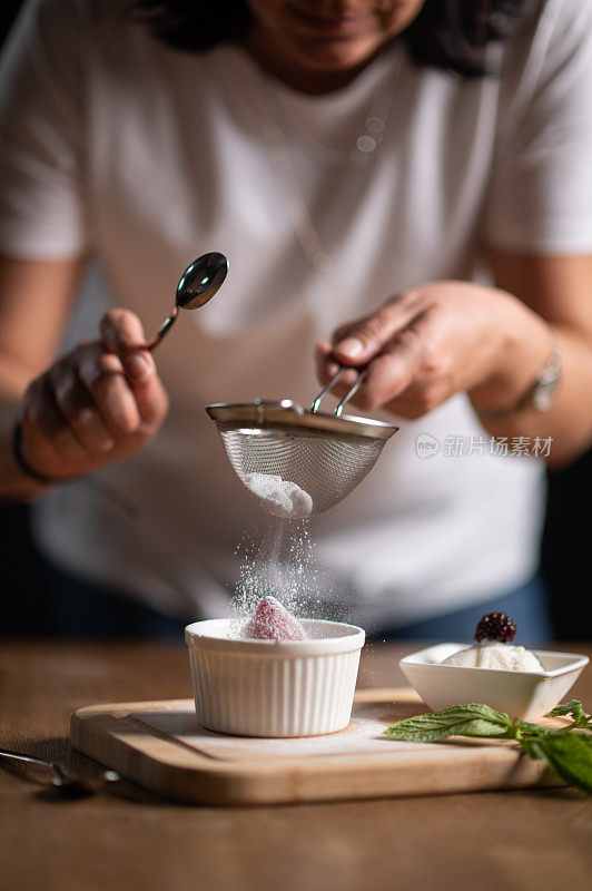 女厨师在巧克力舒芙蕾上撒糖粉