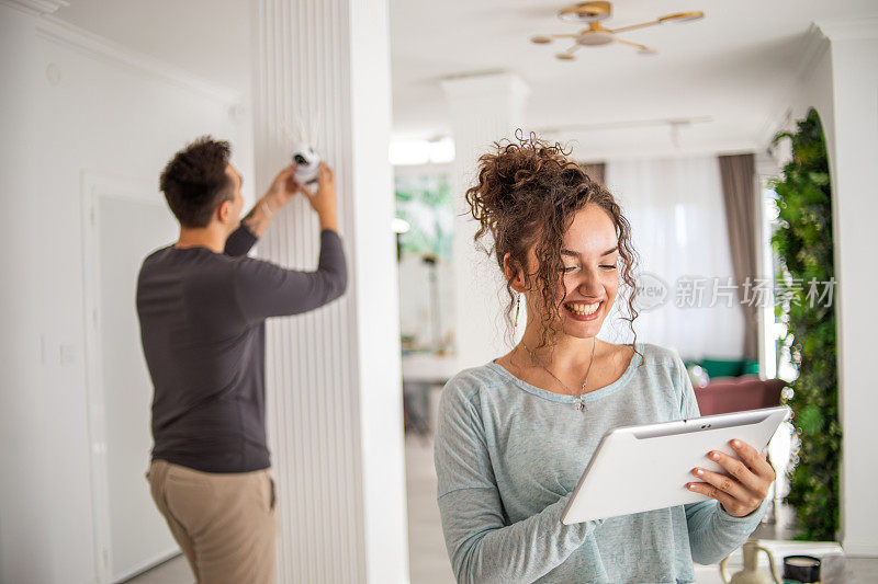 一对年轻夫妇，一男一女，正在他们的公寓里安装家庭监控摄像头