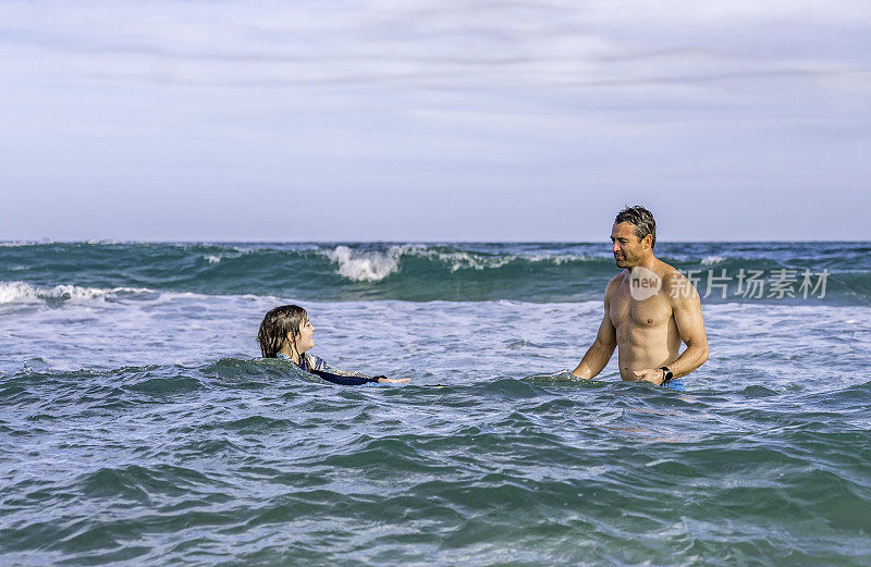 在一次热带度假中，爸爸和女儿一起玩耍，教她如何在海里冲浪