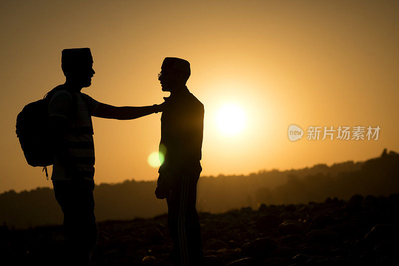 两个年轻人站在夕阳的映衬下。