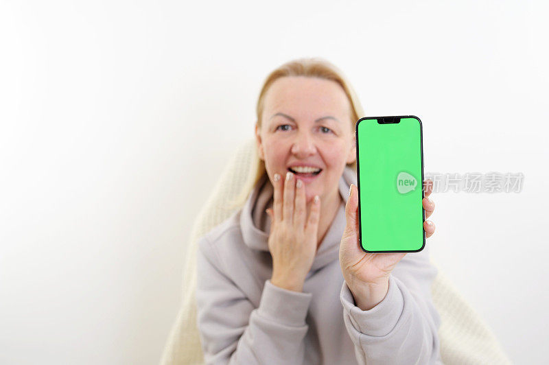 一名年轻女子脸上露出惊讶的表情，手指着她手中绿色屏幕的智能手机。