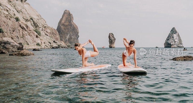 女人喝瑜伽。快乐的运动女性在桨桨冲浪板上练习瑜伽普拉提。女性在海水中做伸展运动。现代女性个人潮人户外夏季体育活动。