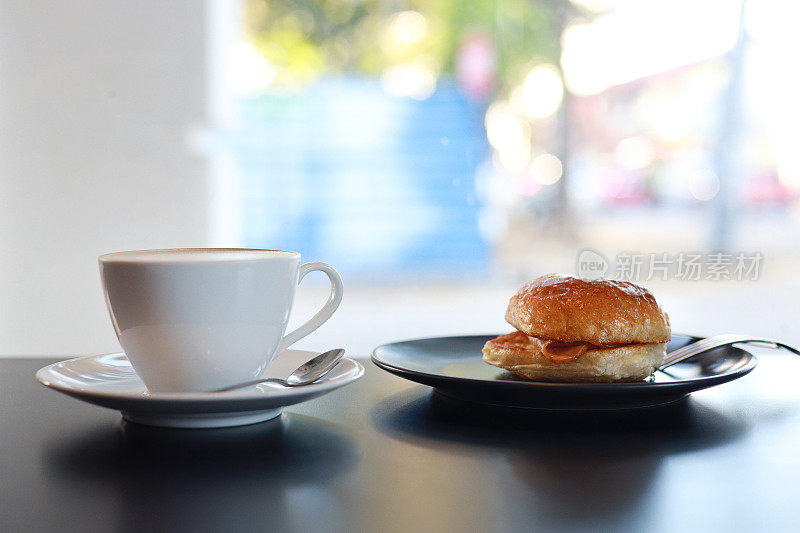 一杯卡布奇诺拿铁和百吉饼放在咖啡馆靠窗的桌子上