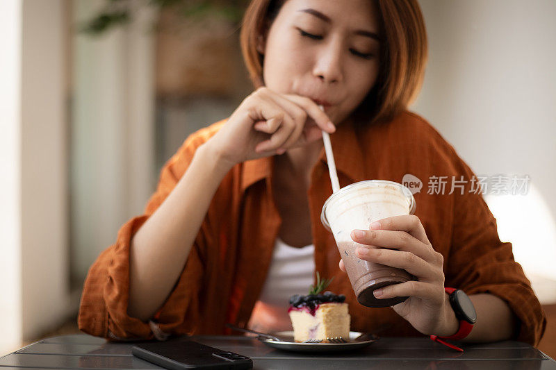 穿着黄衬衫的快乐女士坐在桌边喝着冰巧克力饮料。