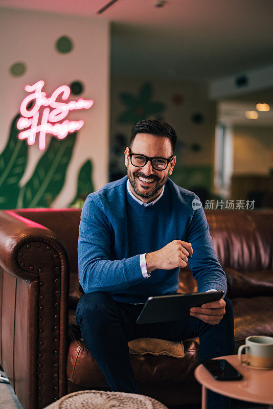 一个快乐的商人，在数码平板电脑前工作，喝着咖啡。