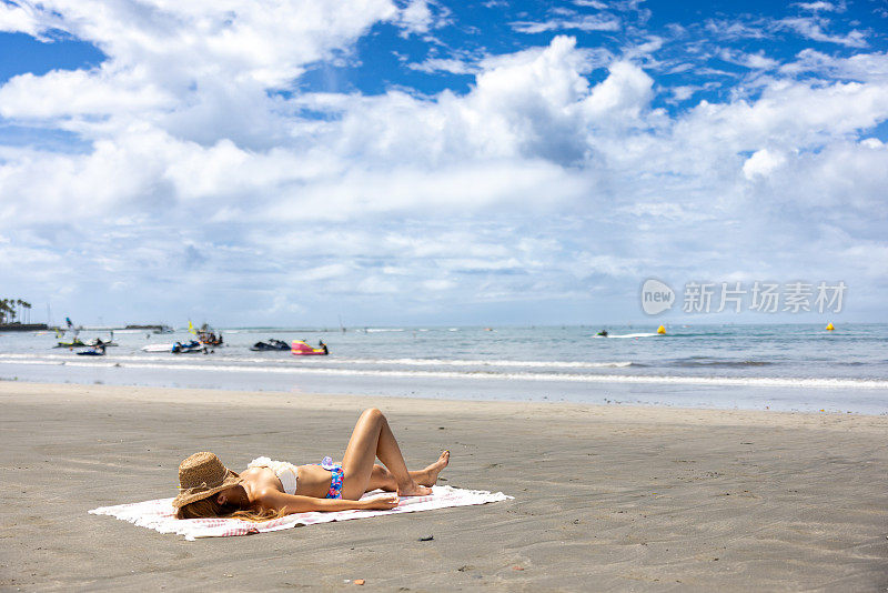 夏日沙滩上，身穿比基尼的女子仰面躺着