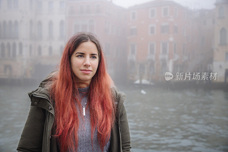 一个雾蒙蒙的冬日，美丽的年轻女子站在意大利威尼斯大运河旁