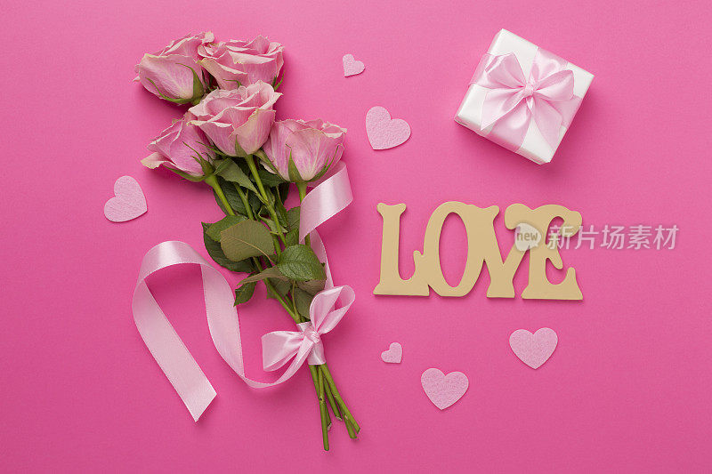 粉红色玫瑰与心和礼盒的颜色背景，俯视图。情人节概念