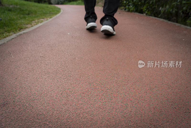 一个穿着运动鞋的男人站在红色的田径跑道上，特写