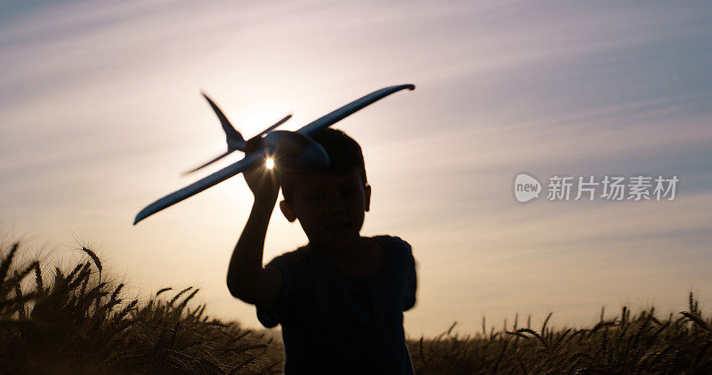 夕阳，剪影和男孩用飞机飞翔，童年的发展和自由被小麦。大自然，天空和孩子带着迷你玩具在野外探险，度假和在乡村玩耍