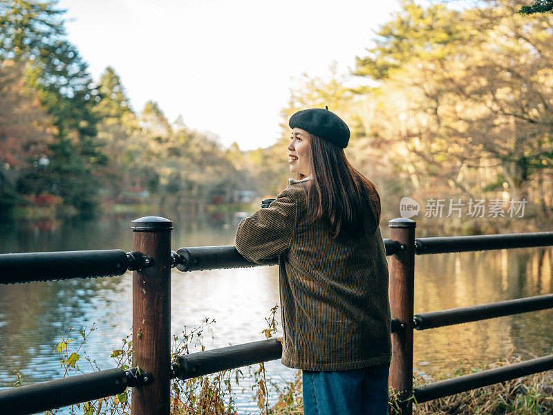 远离混乱，让自己沉浸在大自然的宁静怀抱中。一个亚洲女人站在木栏杆旁，世界隐没在背景中，只留下树叶的沙沙声和水的温柔拍打。