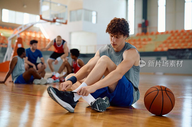 年轻的篮球运动员在球场上系鞋带。