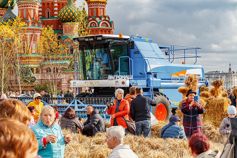 游客在阳光下对抗蓝色的当代联合收割机。莫斯科市中心红场上的传统节日金秋