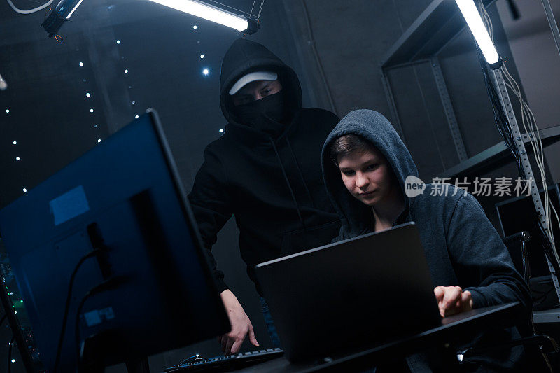 两名黑客看着笔记本电脑的监视器，讨论用来破坏安全系统的新软件代码