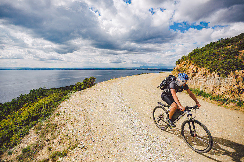 一个年轻人在西班牙的自行车道上骑山地车。运动员骑山地车越野在地中海的背景，科斯塔布拉瓦。骑自行车在西班牙