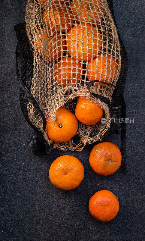 在深色的背景上，自然材料网格上的柑橘类水果。Eco-packaging。明亮的橙色的橘子。自然光线。