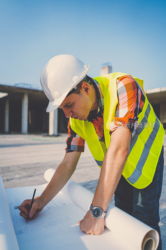 年轻建筑师在建筑工地绘制蓝图