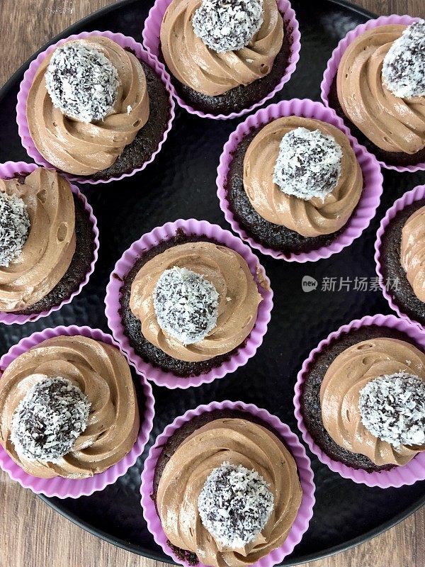 这是自制巧克力纸杯蛋糕的特写图片，上面是管道状的巧克力糖霜和椰子覆盖的松露，紫色的硅胶蛋糕盒