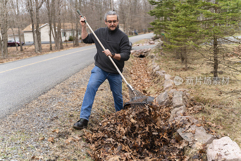 社区志愿服务。一名50岁的男子扎着马尾辫，在春天清理路边的排水沟。