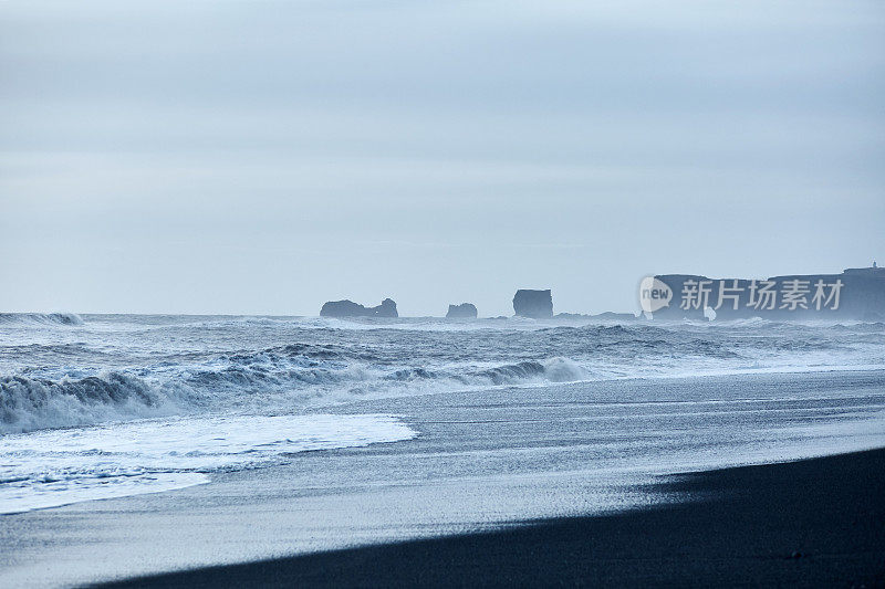 巨大的海浪冲击着海岸，撞击着远处的黑色岩石。冰岛维克的黑沙滩