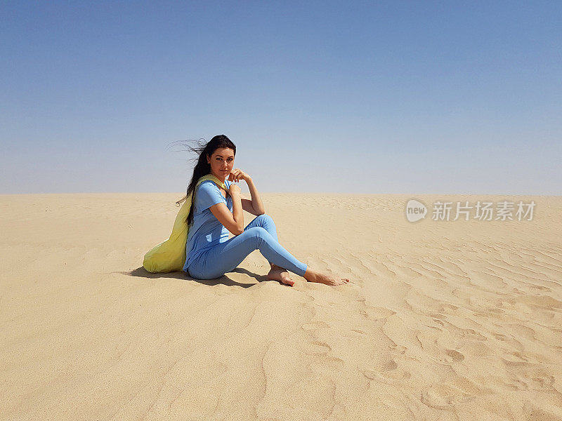 一个年轻女子坐在沙漠的沙滩上。