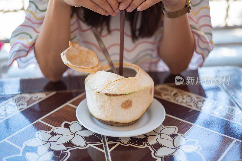 年轻的亚洲女人享受椰子汁在餐厅