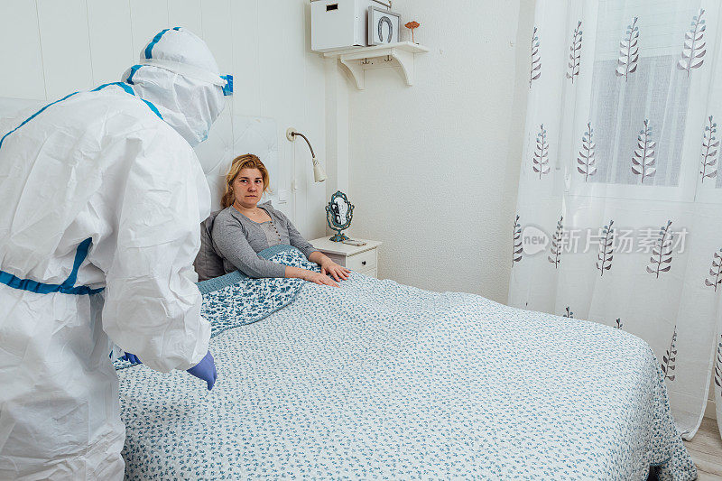身穿个人防护装备的医生在家里的床上照料一位患有冠状病毒的妇女