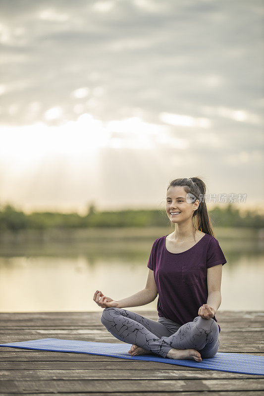 女子练习瑜伽，而坐在莲花位置在湖码头